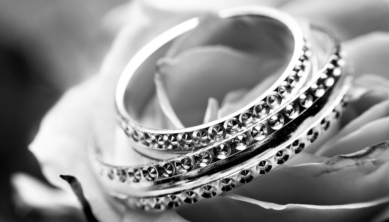 A detailed black and white image featuring ornate rings on a delicate rose, symbolizing elegance and romance.