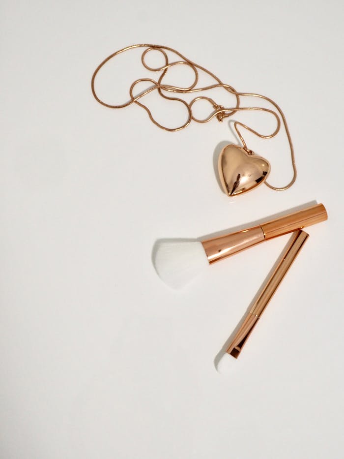 A charming flat lay of a heart-shaped pendant and makeup brushes on a white background, creating a minimalist still life.